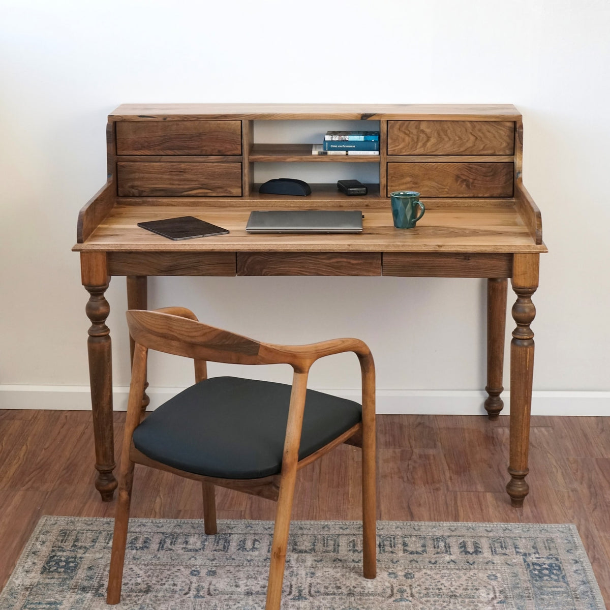 Front view of the walnut desk with hutch and a wood-framed chair with a dark seat on a patterned rug
