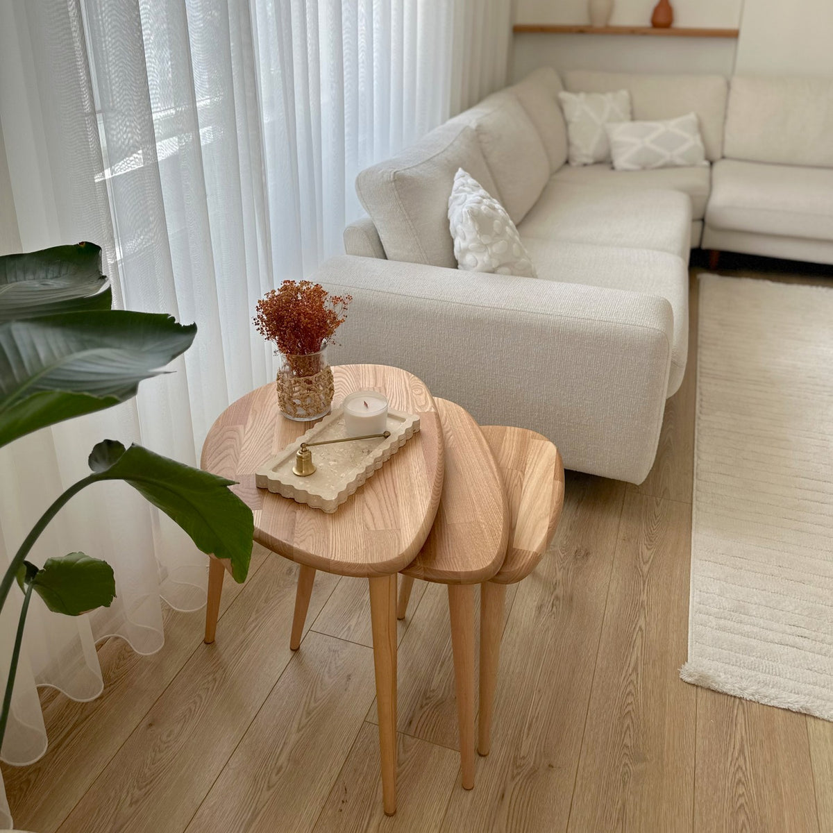 Wide room view of the chestnut nesting table set of 3 in front of a corner sofa
