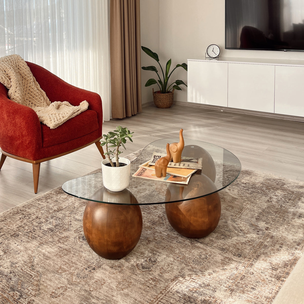 Glass coffee table with spruce ball legs beside a red armchair, seen at a low side angle