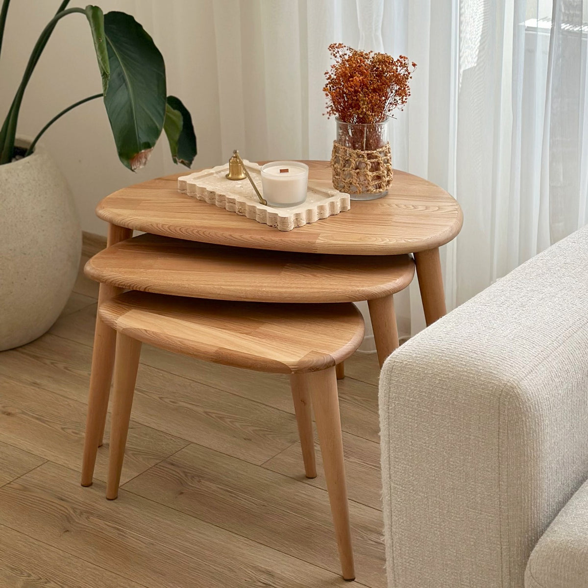 Side view of the chestnut nesting tables stacked together beside a sofa arm