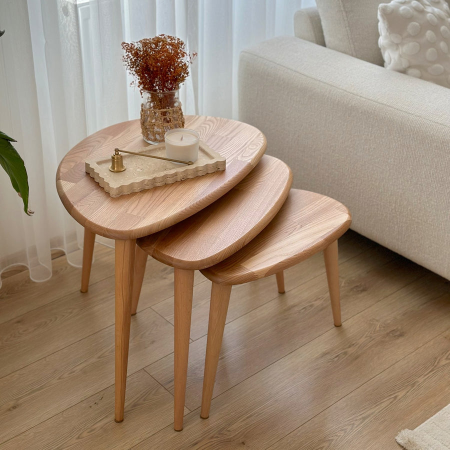 Set of three Ercol style chestnut nesting tables in Transparent-Chestnut color beside a sofa