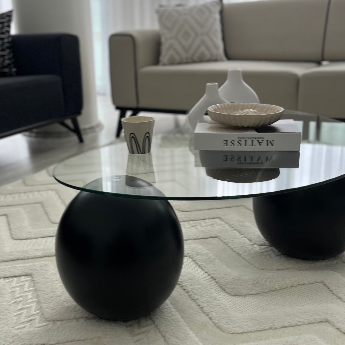 Close-up of a black ball leg under the edge of the round glass coffee table with a stack of books on top