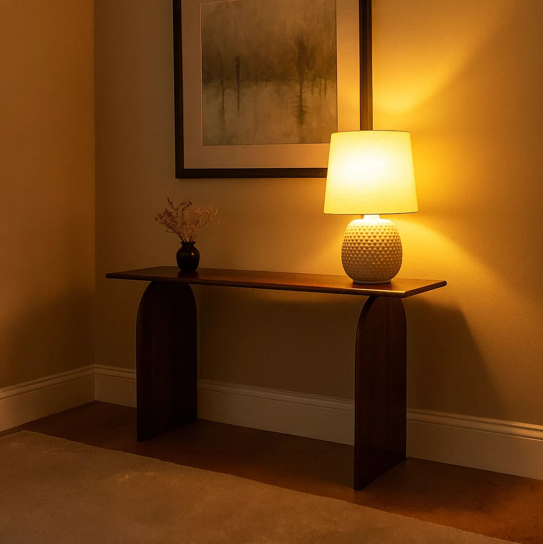 Dark walnut console table in a warm-lit corner with a glowing lamp and a small vase
