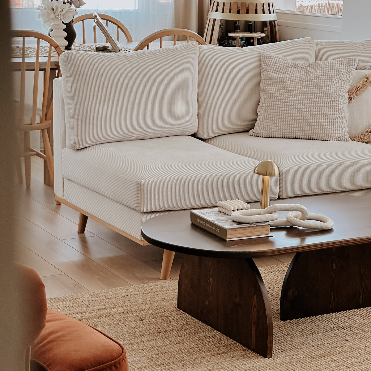 Oval Japandi coffee table in dark brown seen from a low angle in front of a beige sofa