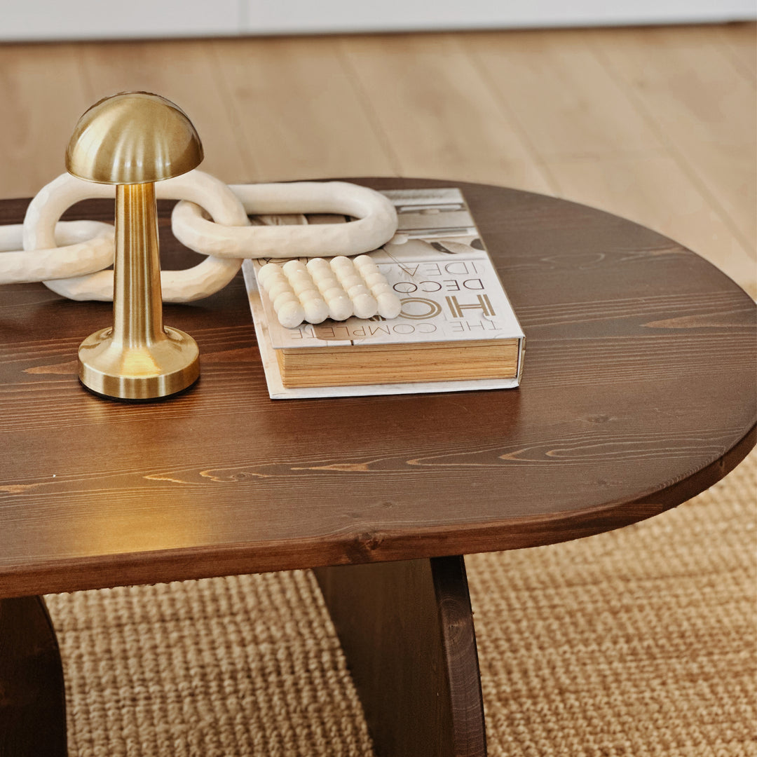 Decorative items on a wooden table with a book and a gold lamp.