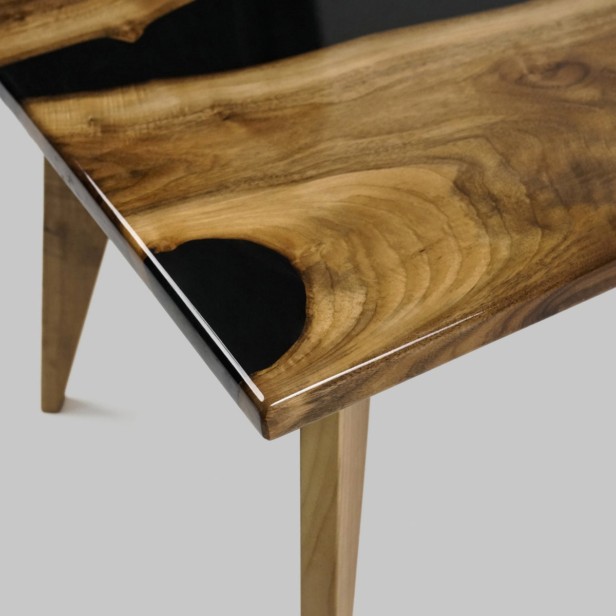 Close-up of the walnut slab edge and black epoxy pocket at the coffee table corner, gray backdrop