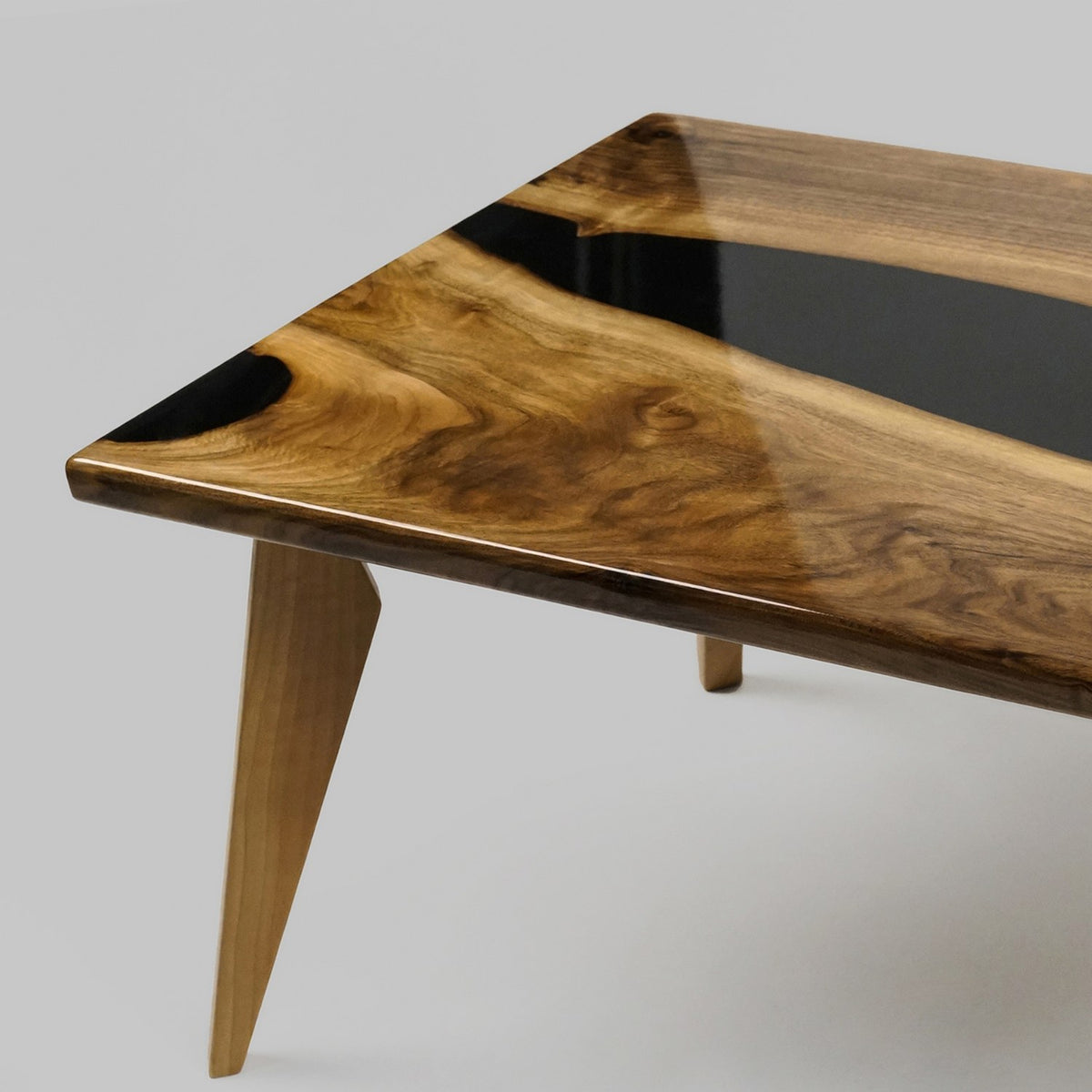 Corner of the walnut live edge coffee table with black epoxy and a tapered leg on a gray backdrop