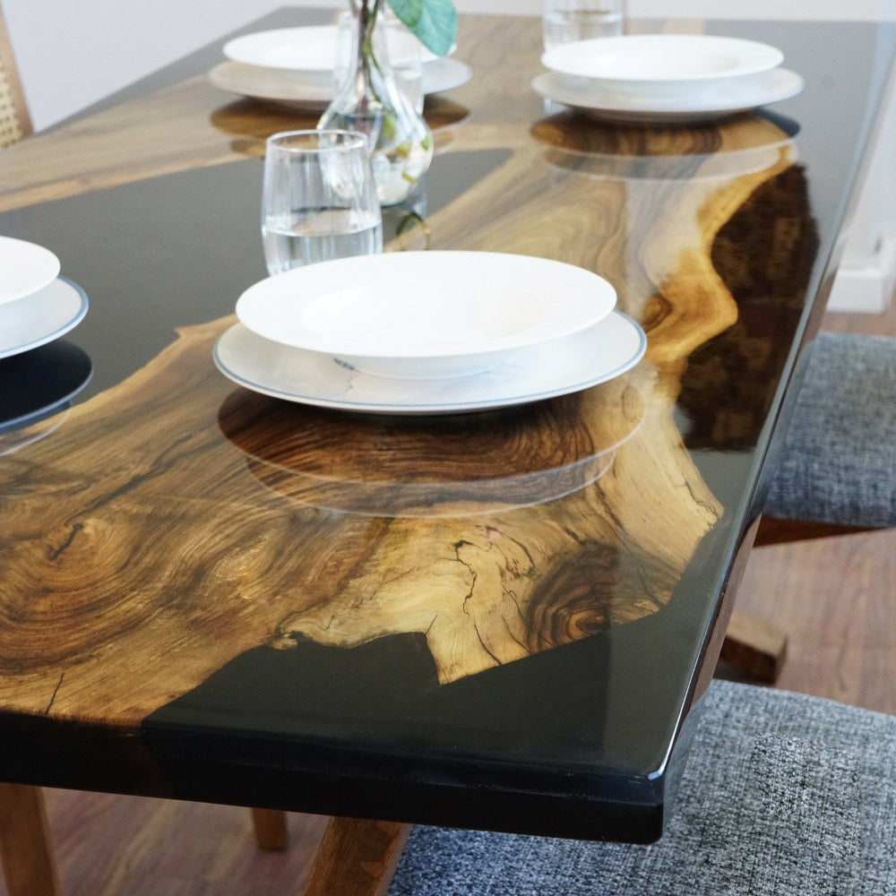 Close-up of the live edge walnut slab edge and black epoxy river with plates on the black walnut table