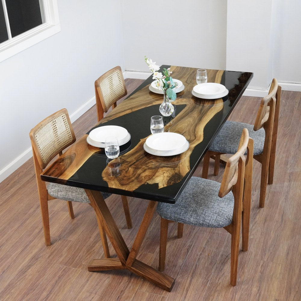 High corner view of the black walnut live edge dining table with a black epoxy river and four rattan back chairs