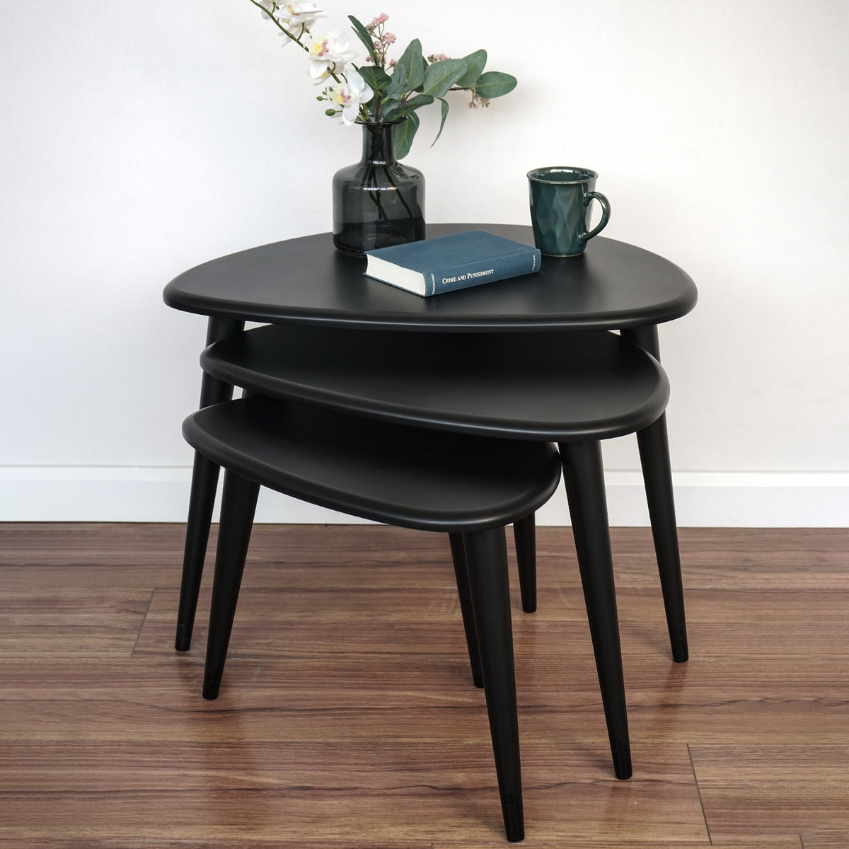 Front view of the matte black Ercol Pebble style nesting table set of 3 against a white wall
