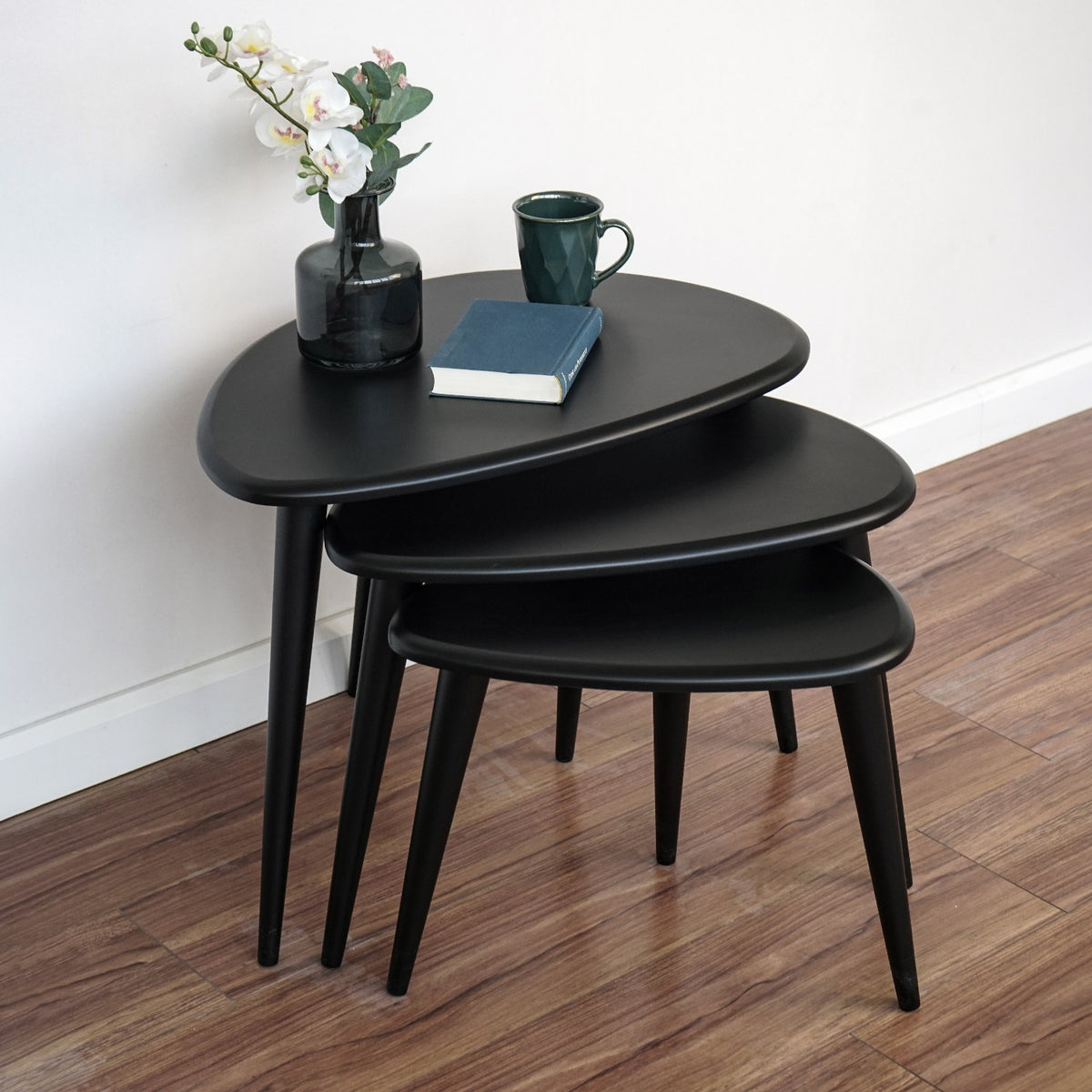 Three-quarter view from above of the matte black nesting tables nested together on a wood floor