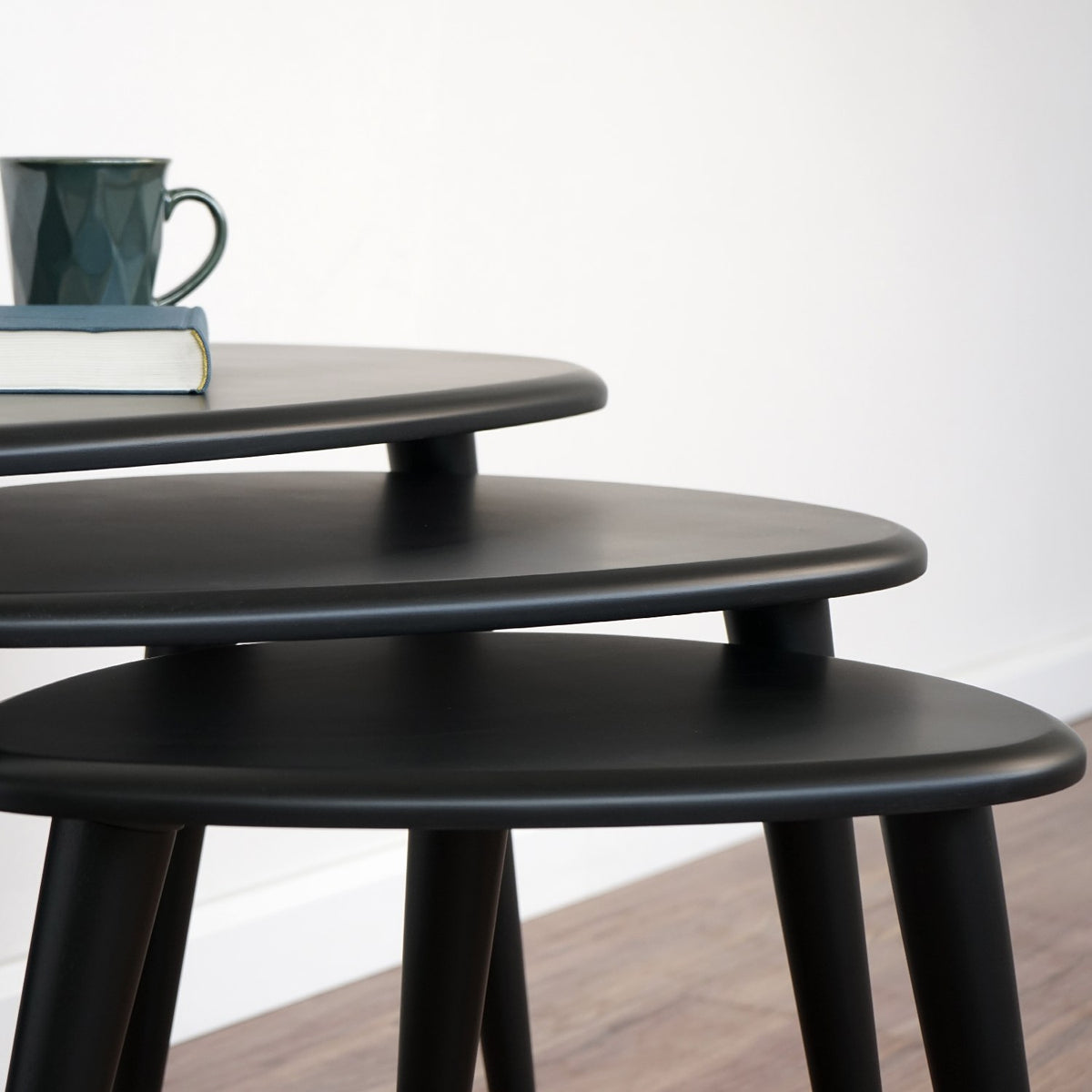 Close-up of the stacked matte black tabletops and the tops of the tapered legs on the nesting set