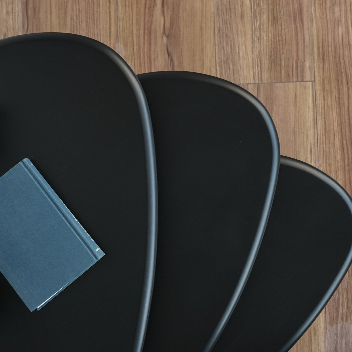 Top-down close-up of three matte black tabletops fanned out over a wood floor