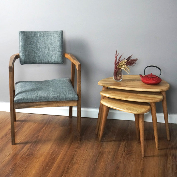 Natural oak pebble nesting tables stacked beside a gray upholstered armchair