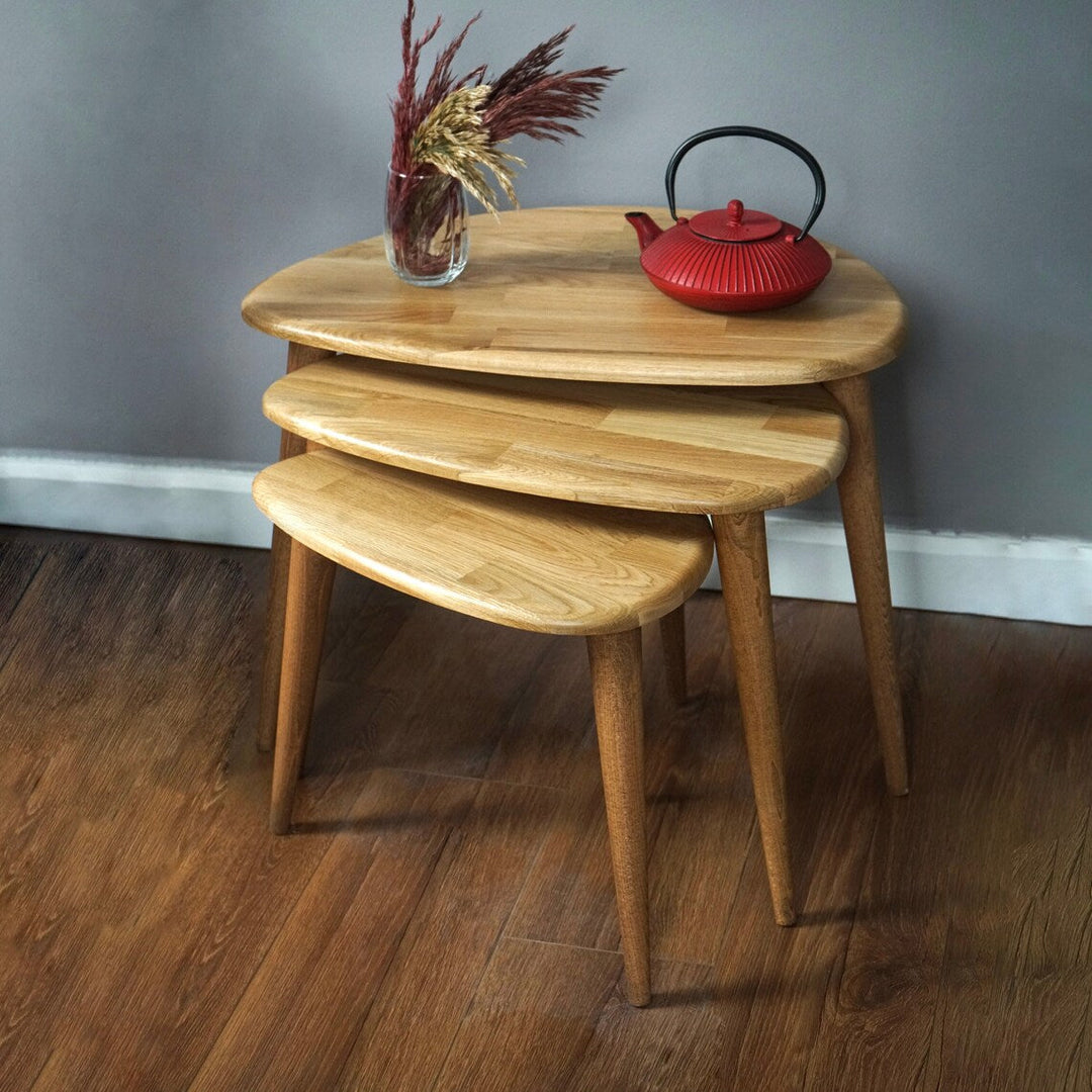 Natural oak nest of three pebble tables against a gray wall, with a red teapot on the top table