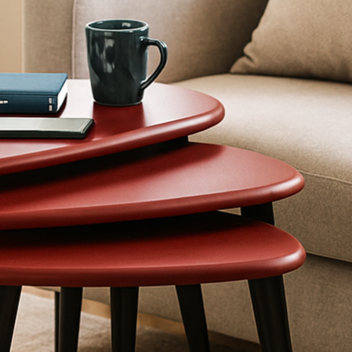 Stack of red nesting tables with a black mug and phone on top, against a beige sofa.