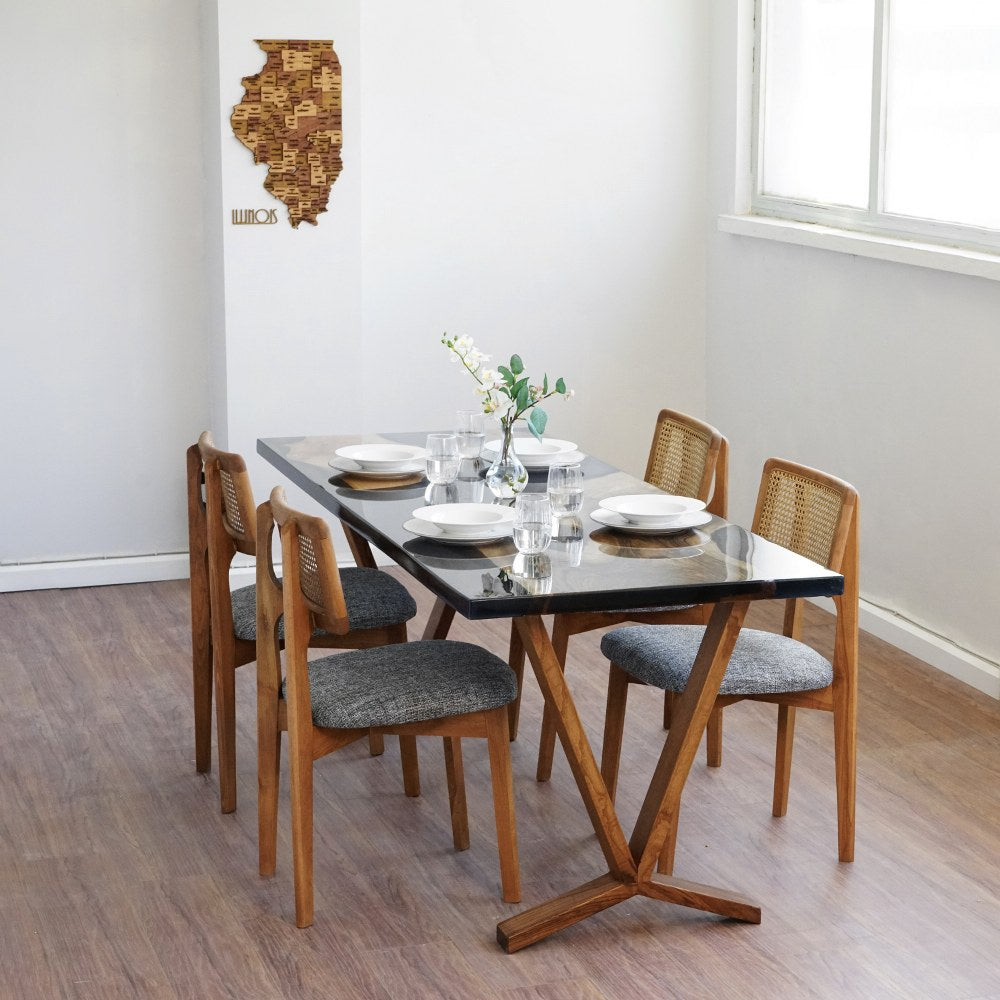 Obsidian black epoxy dining table seen from the far corner of a white room with four rattan back chairs