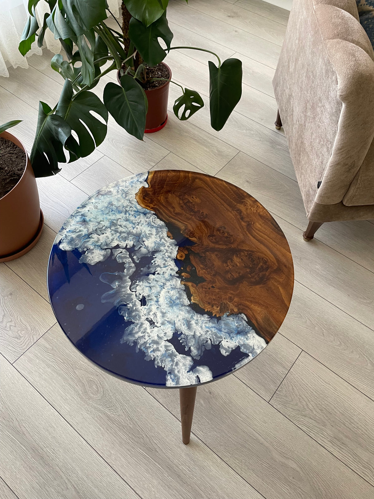 Top view of the round oleaster table with brown live edge wood and blue epoxy with white wave details, near a plant
