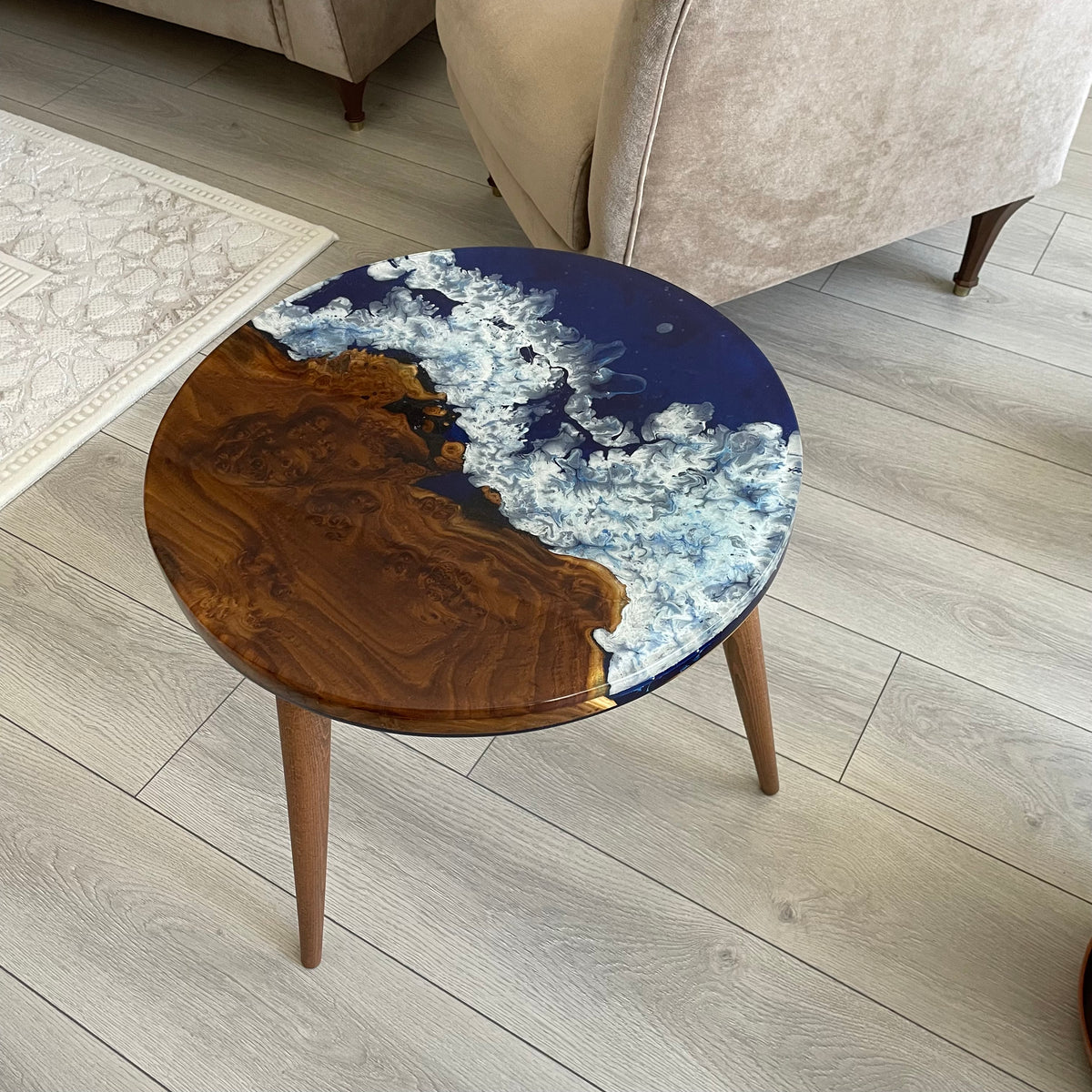 Round oleaster side table with a dark live edge wood section and blue epoxy sea, on three tapered legs
