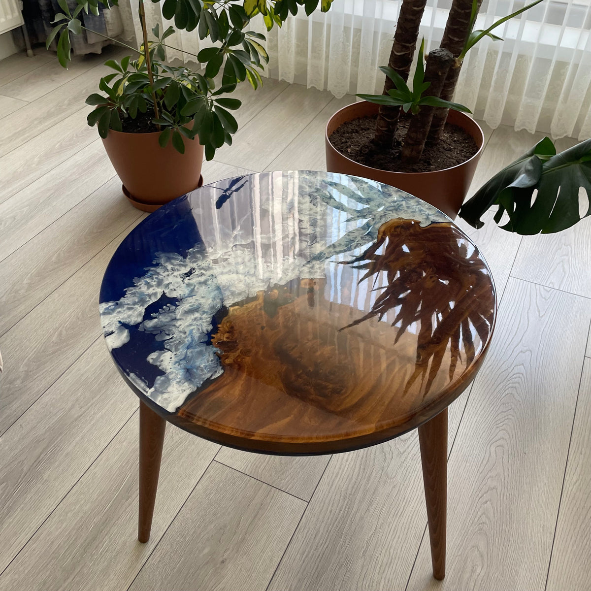 Round oleaster side table seen from the front, brown tapered legs and a blue epoxy sea top