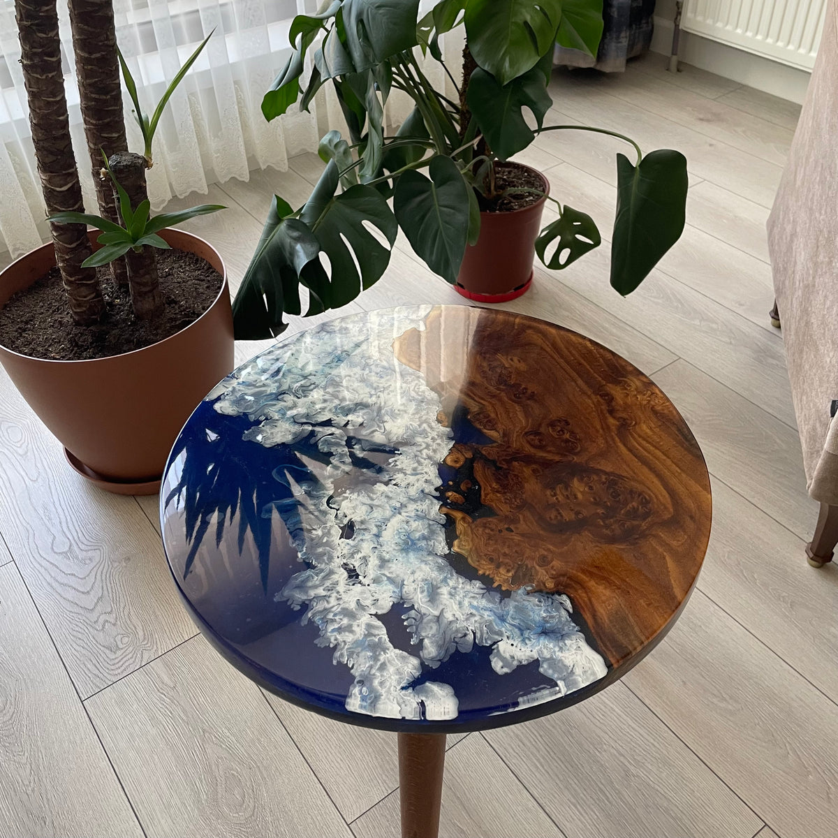 Glossy ocean blue epoxy tabletop with a live edge oleaster slab, with leaves reflected in the resin