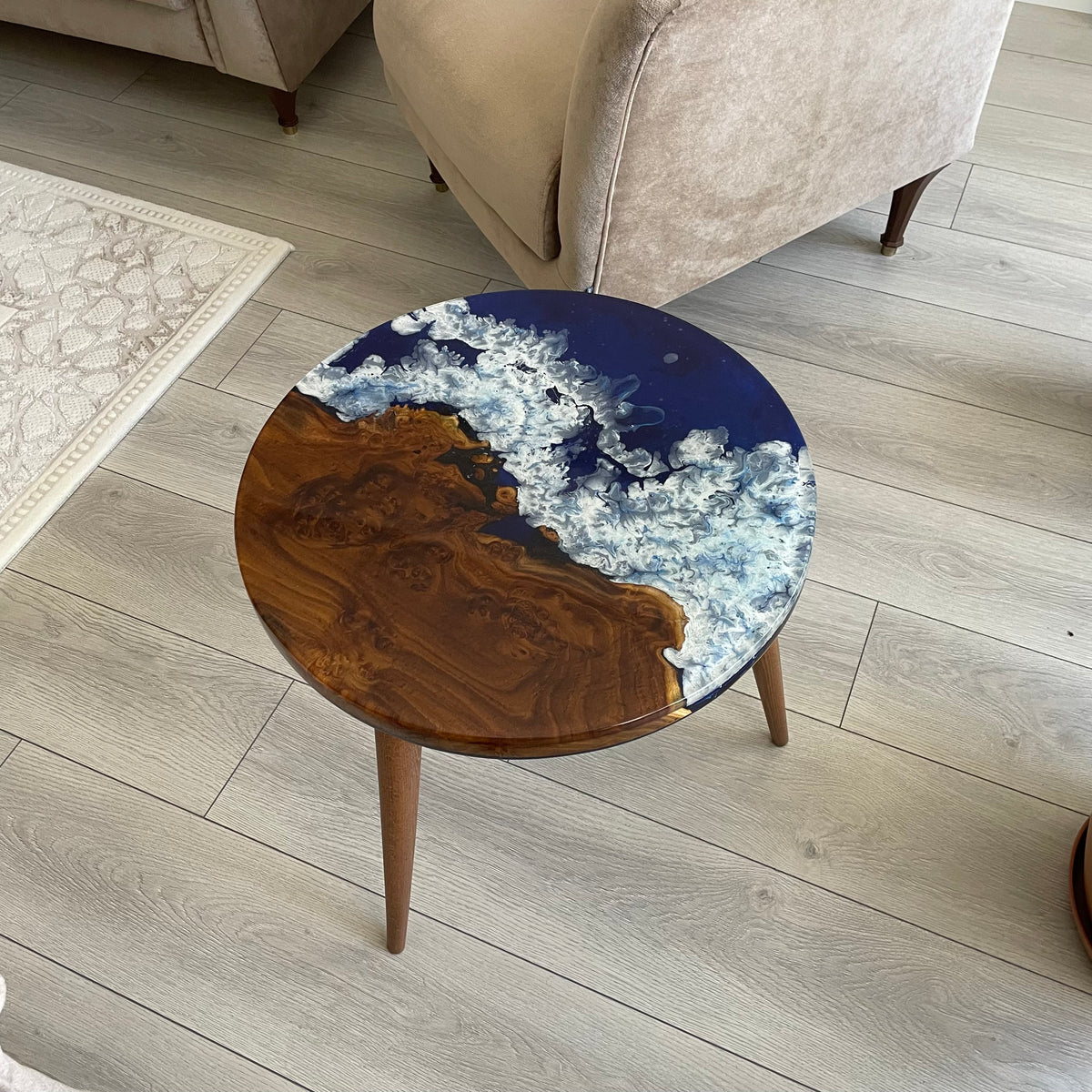 Round oleaster side table with an ocean blue epoxy river and white wave foam on a gray wood floor