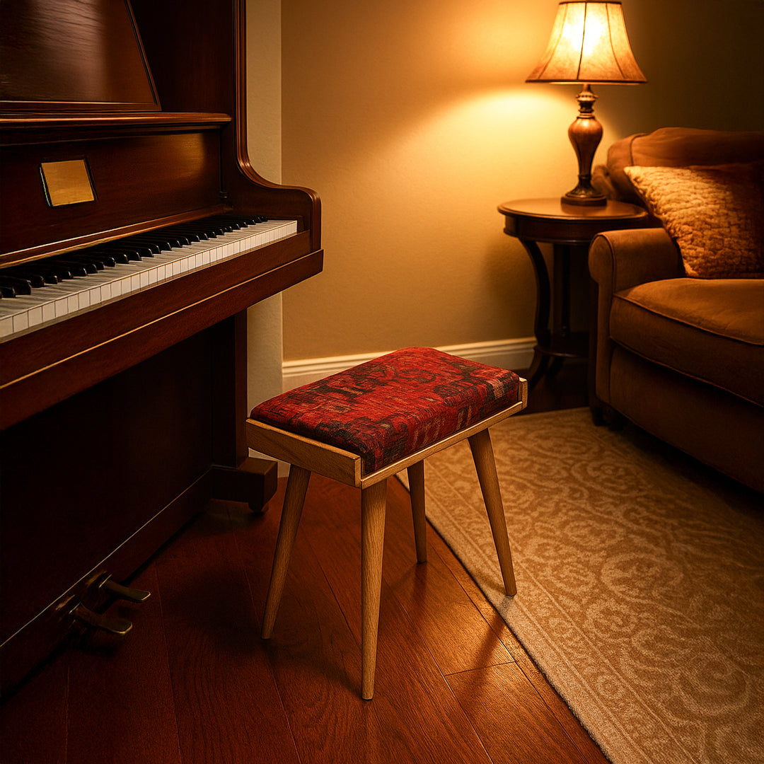 Wooden piano with a red cushioned stool in a warmly lit room.