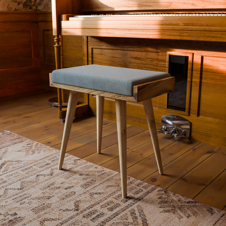 Wooden stool with a cushion in front of a wooden piano on a wooden floor.