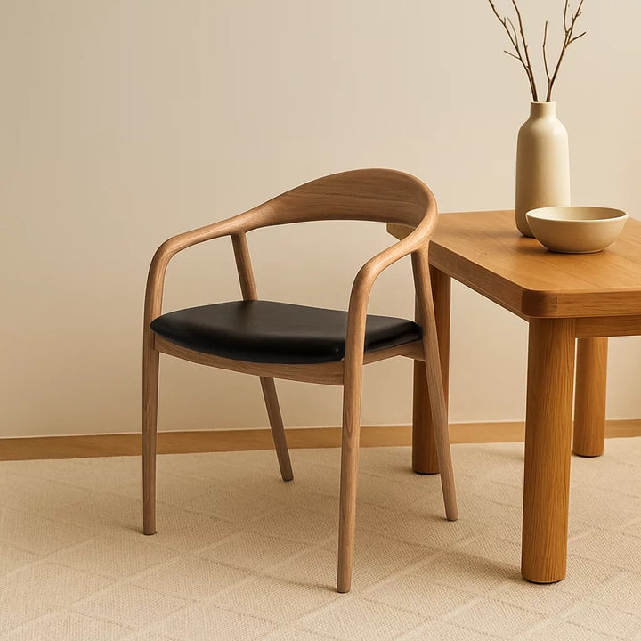 Solid wood beech dining chair with black leather cushion beside a table and a vase in a cozy room setting.