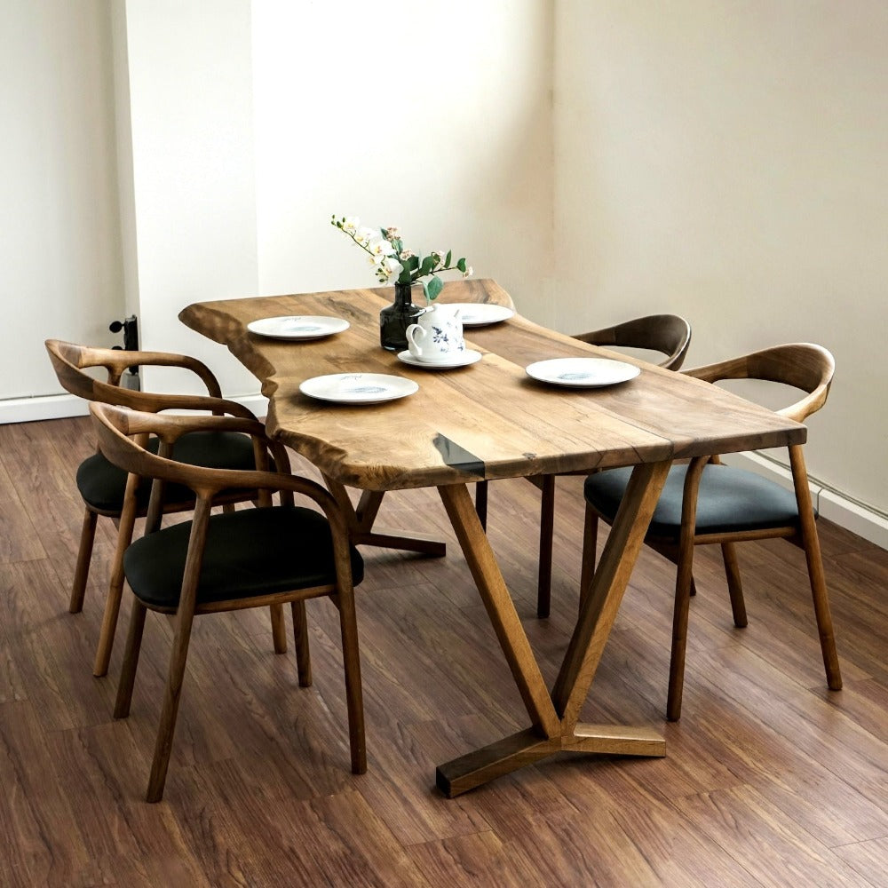 Walnut live edge farmhouse table seen from the left with a V-shaped base and black-seat chairs