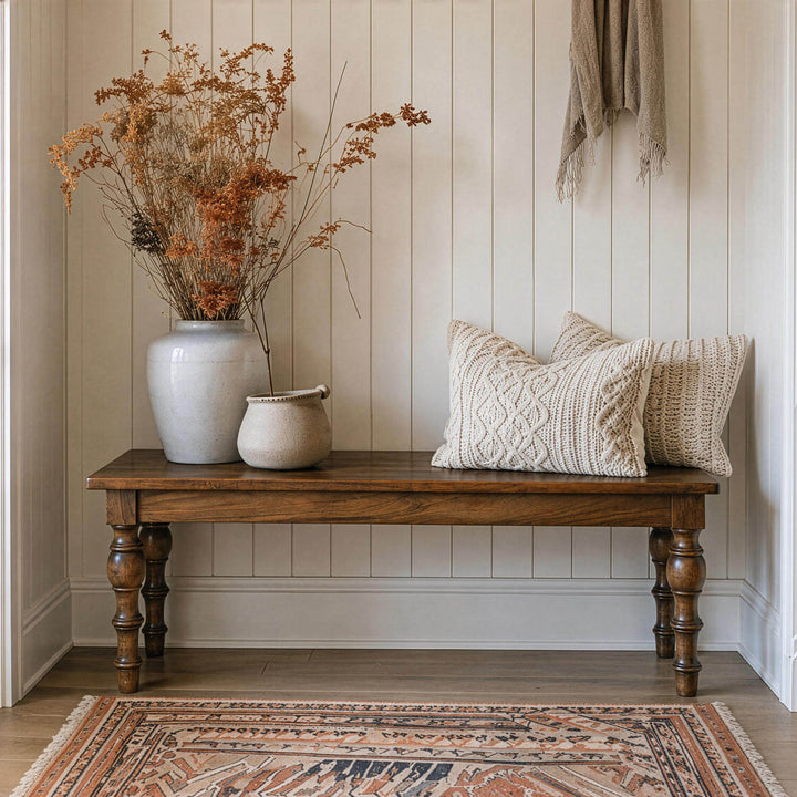 Turned leg wooden bench decorated with textured knit pillows and rustic ceramic vases in a cozy entryway.