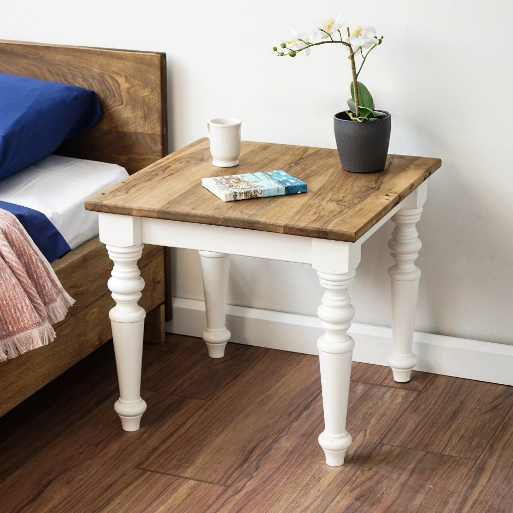 Walnut bedside table with white turned legs next to a bed, wider view showing the bed headboard