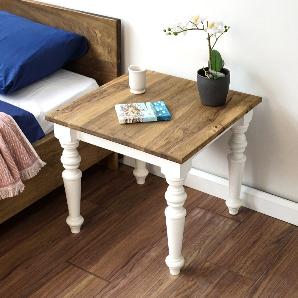 Walnut bedside table with a white apron and white turned legs beside a bed, seen from above at an angle