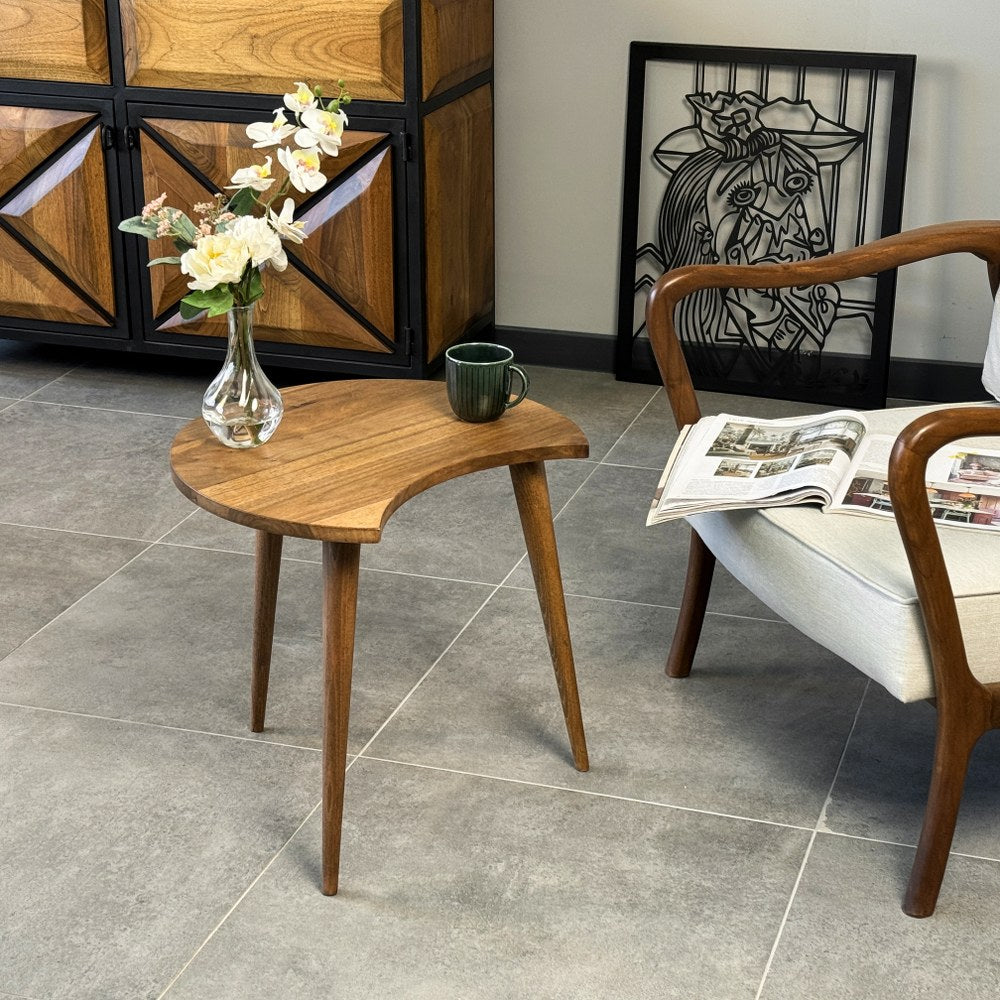 Walnut C-shaped end table beside an armchair, with the open curve facing the viewer and a vase on top