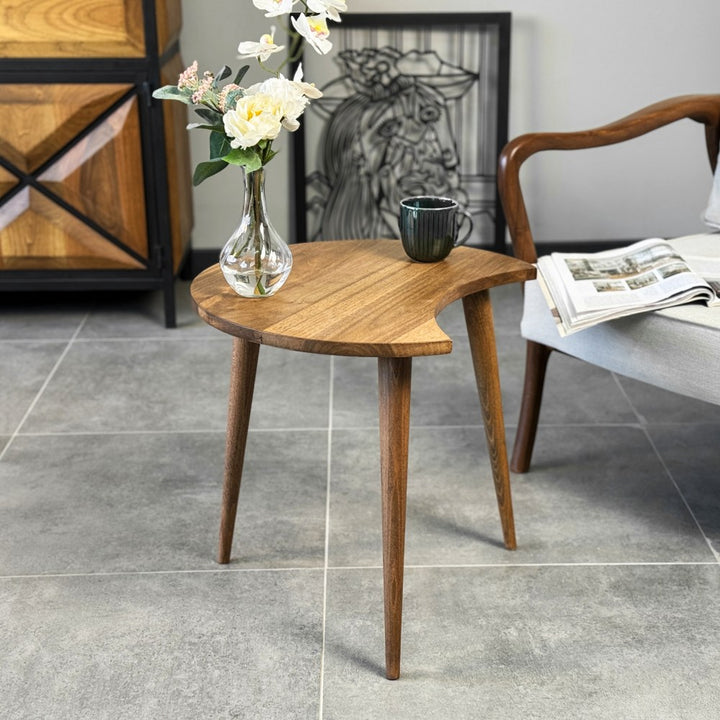Front view of the walnut C-shaped side table showing its three tapered legs, with a vase and mug on top