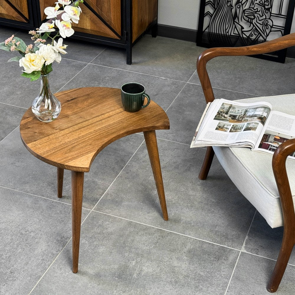 Walnut C-shaped side table with the opening facing an armchair, seen from the front corner