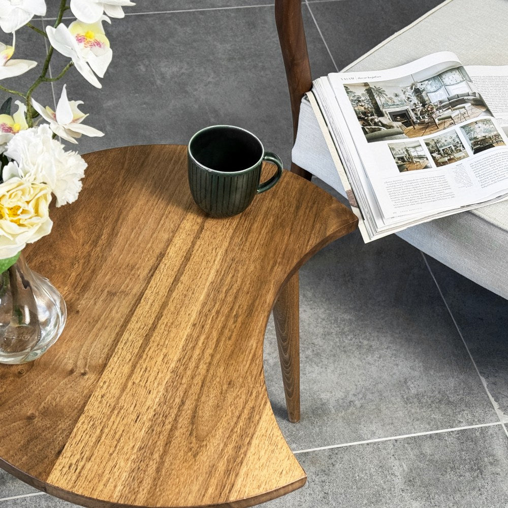 Walnut C-shaped side table top from above at an angle with a mug and a magazine on the armchair