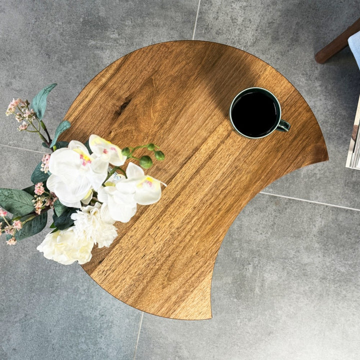 Top-down view of the C-shaped walnut side table with a mug and a white orchid arrangement
