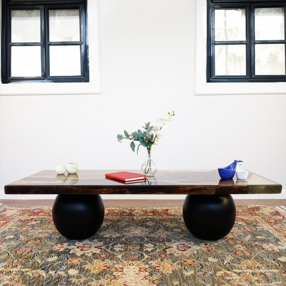 Straight front view of the walnut epoxy coffee table on two black ball legs against a white wall
