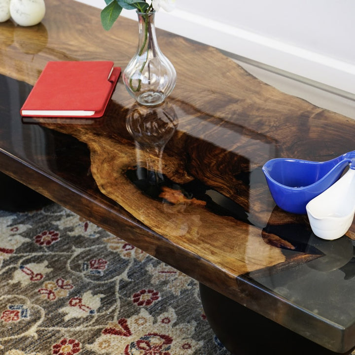 Close-up of the epoxy-filled walnut slab and clear edge of the coffee table above a black ball leg