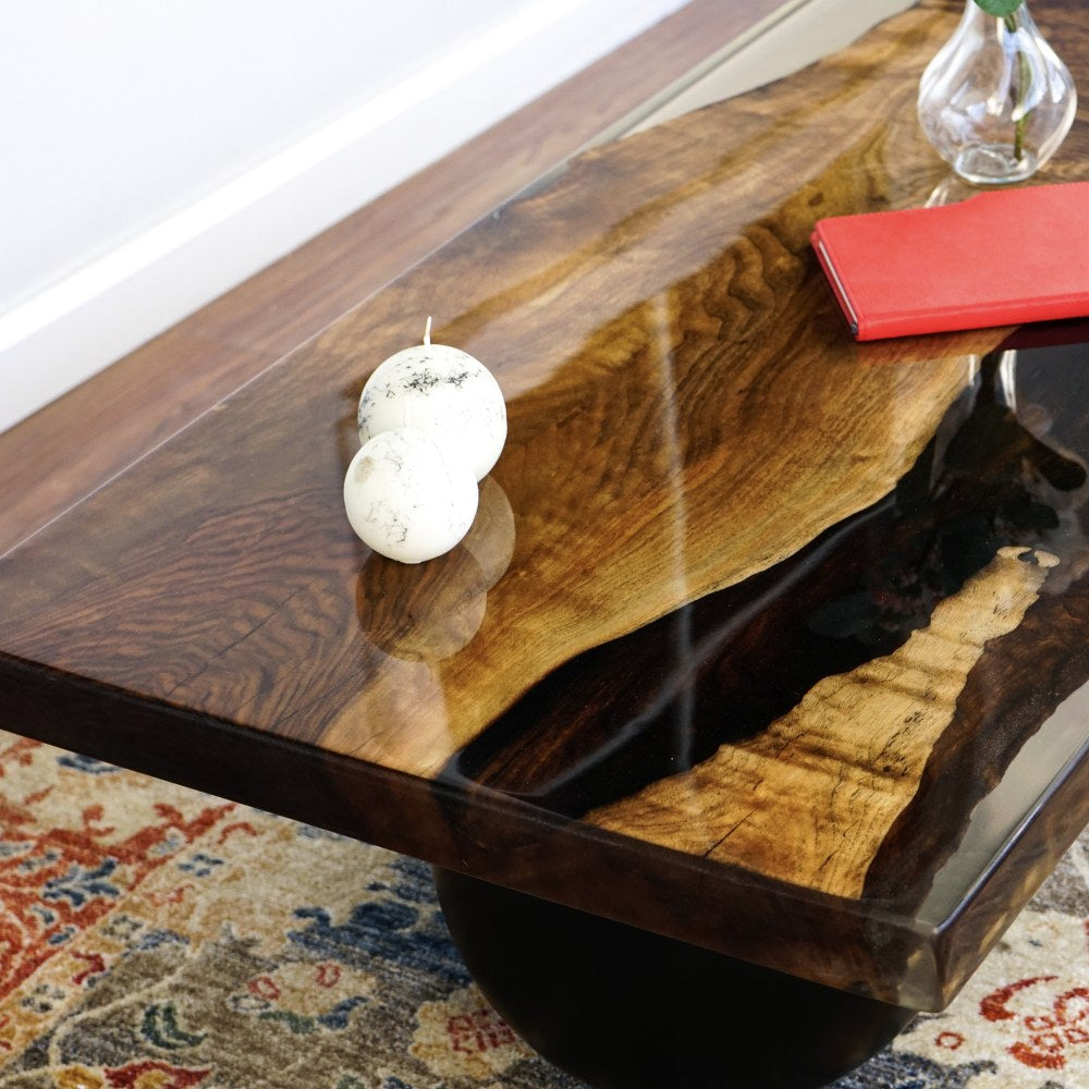 Close-up of the walnut live edge and dark epoxy river on the coffee table top, black ball leg below