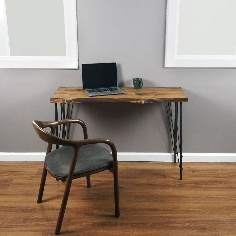 Solid walnut live edge desk with black hairpin metal legs, front view with a laptop and a wood armchair