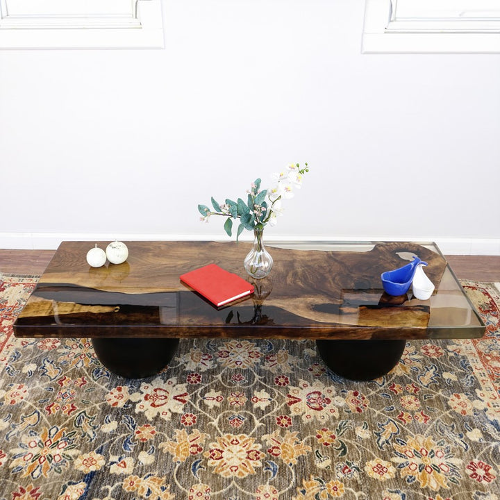 Front view of the live edge walnut epoxy coffee table on two black wooden ball legs on a patterned rug