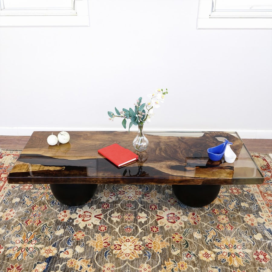 Front view of the live edge walnut epoxy coffee table on two black wooden ball legs on a patterned rug