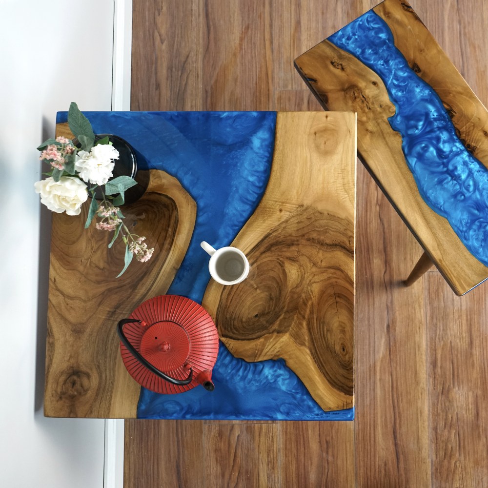 Top view of the walnut nesting tables with blue epoxy river, a tea cup, red teapot and flowers on the large table