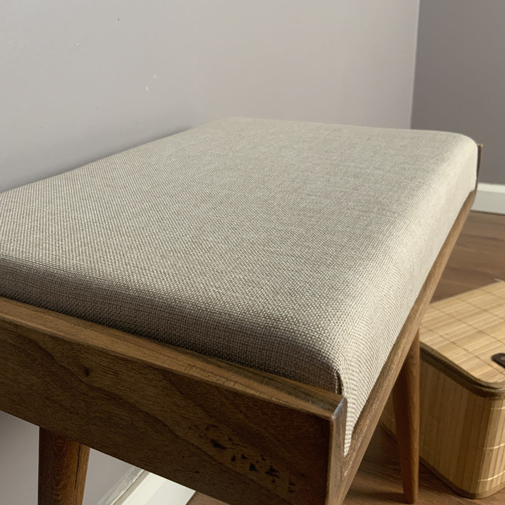 Close-up of the cream upholstered seat and walnut frame edge of the piano bench
