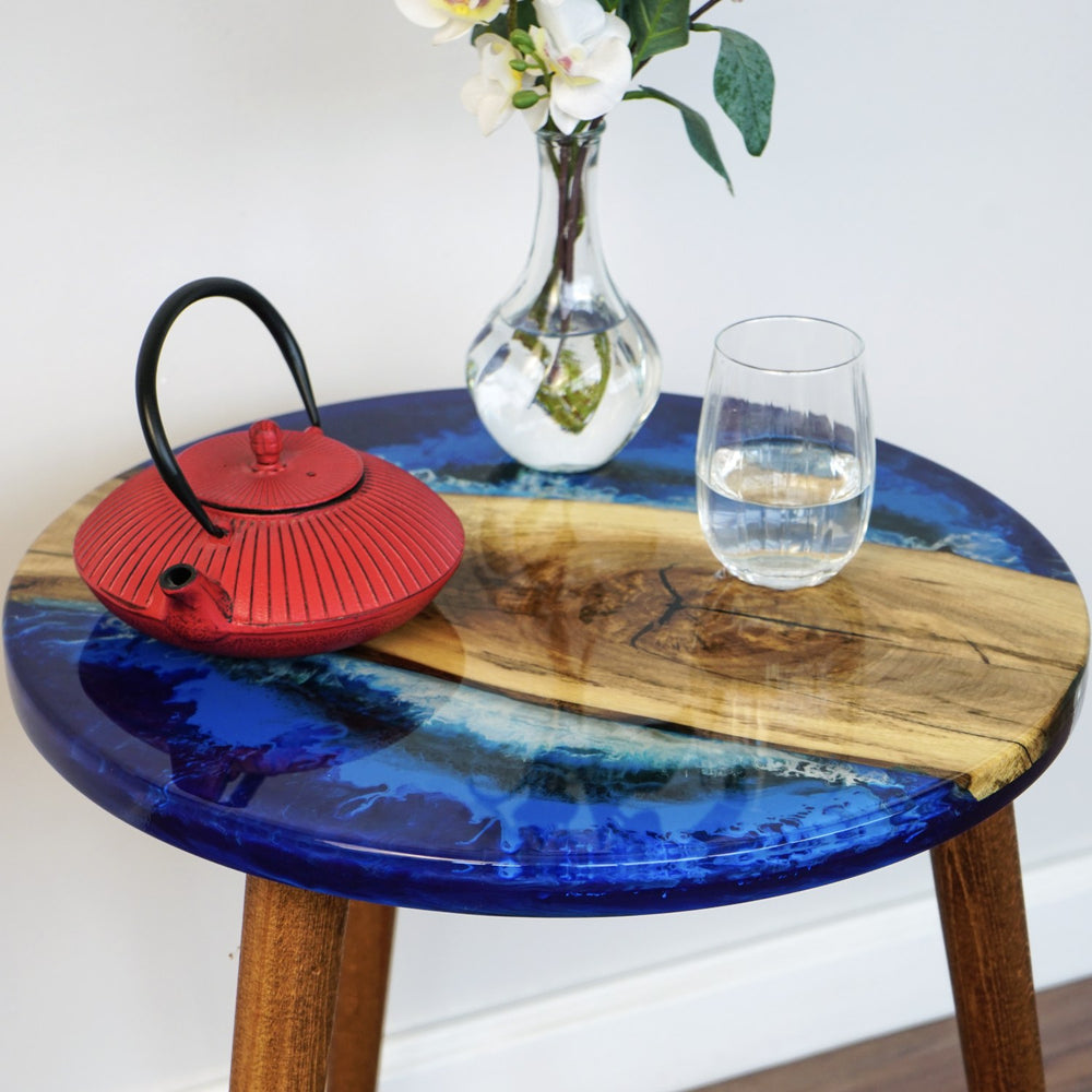 Close-up of the Sea Design blue epoxy and live edge walnut on the round side table, with a glass of water