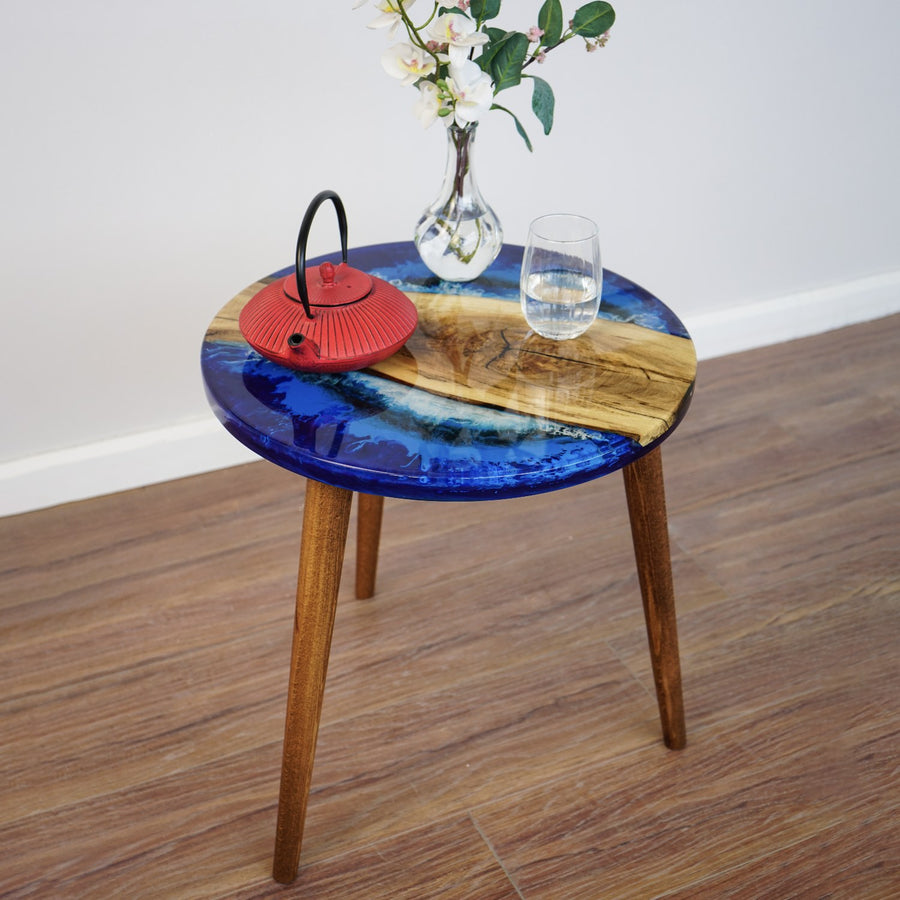 Round live edge walnut side table with Sea Design blue epoxy and tapered legs, mid-distance view