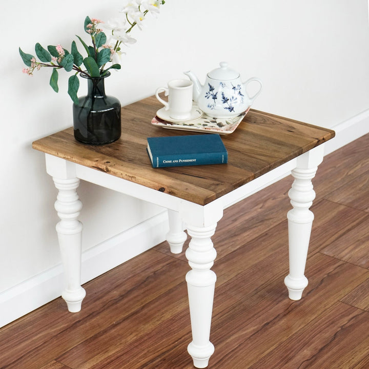 Walnut side table with white legs on a hardwood floor against a white wall, corner view