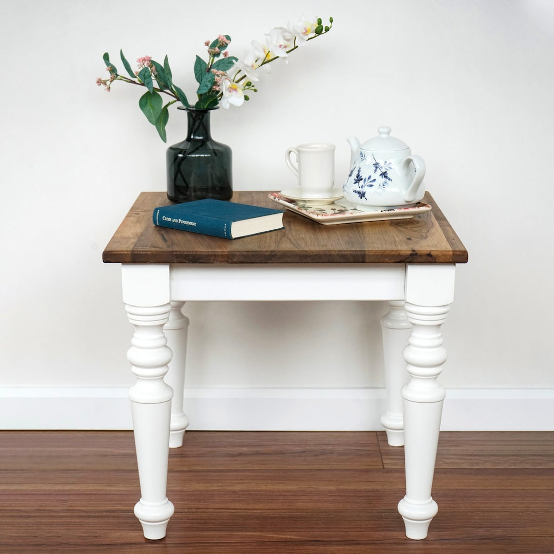 Farmhouse walnut side table with white turned legs on a hardwood floor, front view